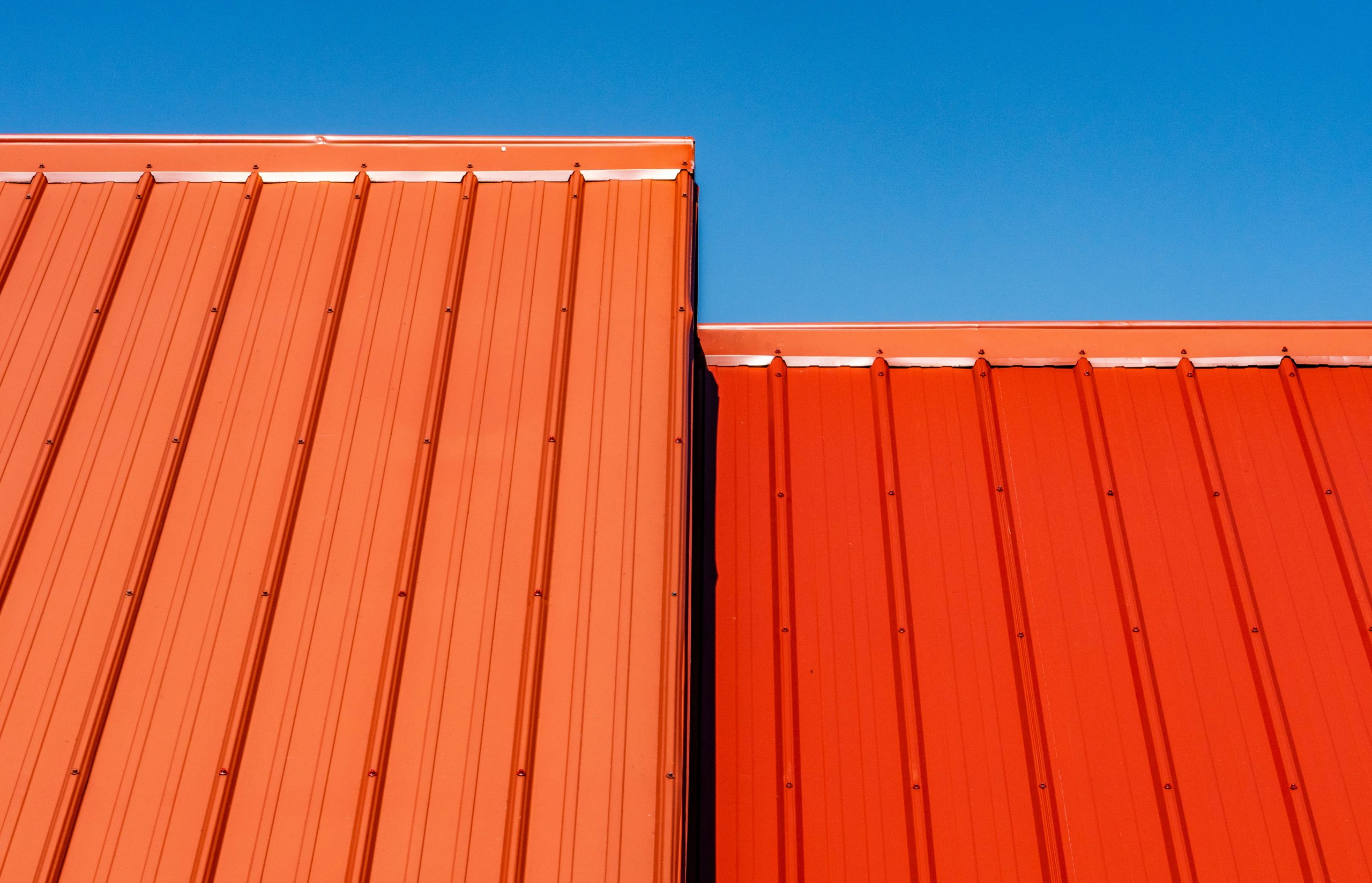 Orange standing seam metal roofing panels against a blue sky
