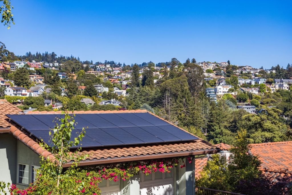 Southern California hillside home with a clay tile roof and a row of black solar panels under a blue sky